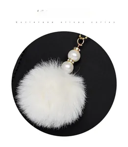 Detailed macro view of white fluffy pom-pom charm with pearls on a black leather bag