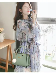 Light green leather handbag with white pompom charm carried by model in floral dress