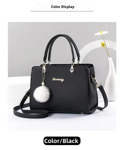 Detail of black faux leather handbag with golden logo and white plush ball charm