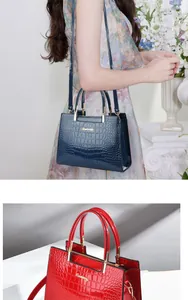 Detail of glossy crocodile pattern handbag with golden logo in navy and red colors