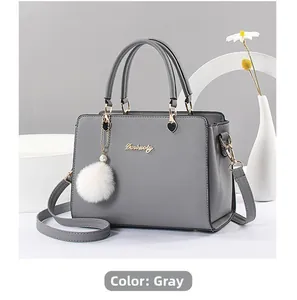 Detail view of grey leather handbag featuring metal heart charm and plush ball accessory