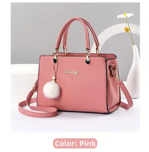Detail of dusty pink leather handbag with a white pompom and gold heart pendant charm