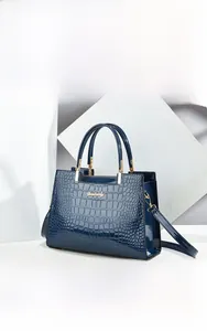 Detail of dark blue crocodile embossed patent leather bag with gold hardware plaque