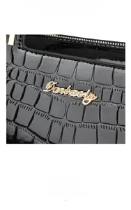 Close-up of black glossy crocodile texture and gold Danbaoly logo hardware on handbag