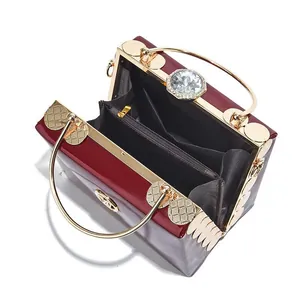 Glossy burgundy patent leather handbag with gold round handles and crystal clasp