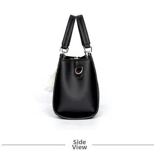 Side view of a black leather bucket handbag with two handles and a white plush ball charm