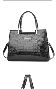 Detail view of glossy black crocodile pattern handbag with gold logo and handles