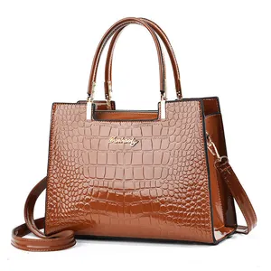 Detail of glossy brown crocodile embossed leather handbag with golden logo and textures