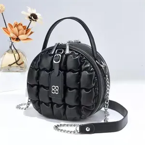 Detail der schwarzen gesteppten Rundtasche mit Doppelreißverschluss und Lederanhänger