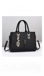 Close-up of black handbag with geometric quilting, pearl leaf charm, and gold hardware