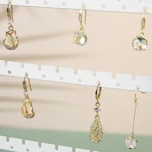 Detalle de pendientes dorados con tulipanes y perlas en un soporte blanco para joyas