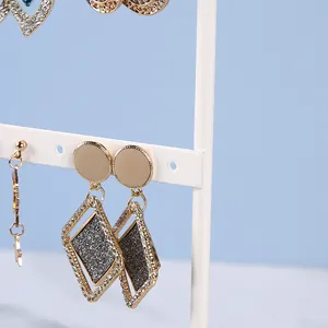 Detail of geometric earrings with black glitter and rhinestones on a white metal jewelry stand