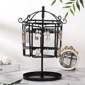 Rotating black iron jewelry stand with earrings on a marble surface near a mirror