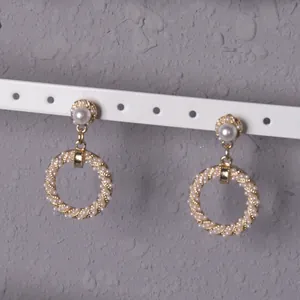 Primer plano de pendientes vintage redondos dorados con textura trenzada y perlas