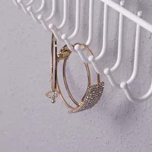 Detalle de aretes de aro dorados con dijes geométricos de diamantes en soporte blanco