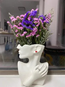 Detail of white ceramic bust vase with red heart earring and purple floral accent