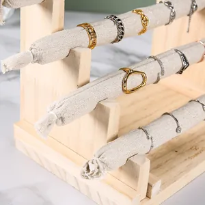 Three-tier wooden ring display stand with beige linen rods showing jewelry on counter
