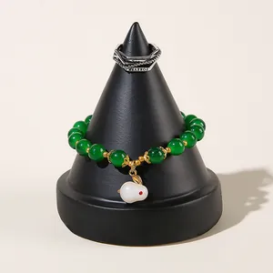 Grünes Perlenarmband mit Hasenanhänger und silbernem Ring auf einem schwarzen Ständer