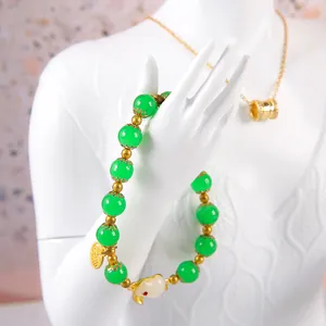 Green beaded bracelet with rabbit pendant and gold charms on white model hand