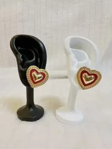 Détail macro de boucles d'oreilles cœur rouge et bord doré sur présentoir en résine