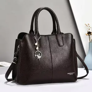 Detail einer dunkelbraunen Handtasche aus Leder mit Perlenanhänger und Metallbeschlägen