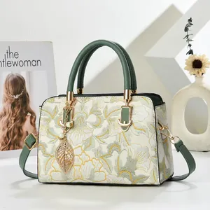 Elegant off-white floral handbag with green handles and gold hardware in a chic setting