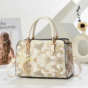 Detail of cream leather handbag with yellow floral embroidery and gold leaf pendant