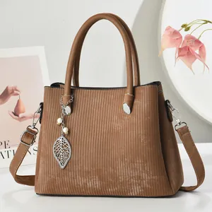 Detail view of brown textured tote bag featuring a leaf pendant and pearl charm