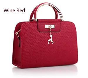 Detail of wine red embossed handbag featuring a textured lychee grain and gold deer pendant