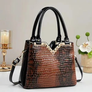 Detail of glossy brown crocodile pattern handbag with gold V-hardware and black patent strap