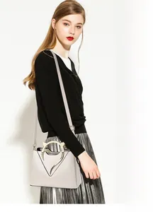 Detail of cream shell bag with cat-ear metal handles and V-shaped metallic trim