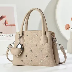 Beige quilted leather tote bag with rivets and heart charm, shown in a cozy home setting