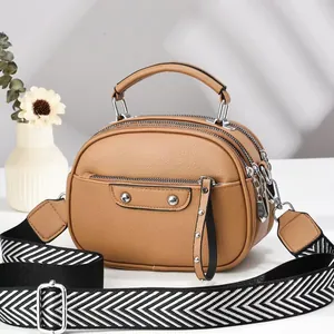 Detail view of brown pebbled leather crossbody bag with three zippers and striped strap
