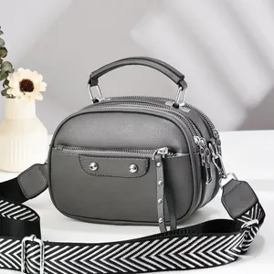 Detail of grey pebble leather crossbody bag with three zipper compartments and wide strap