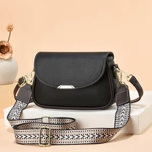 Gros plan du sac en cuir grainé noir avec fermoir doré et bandoulière rayée
