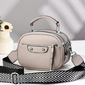 Close-up of beige faux leather crossbody bag featuring triple zip layers and pebble texture