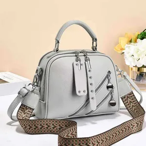 Minimalist light grey leather tote with woven shoulder strap and dual zipper pockets