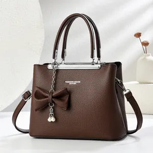 Dettaglio borsa in pelle marrone scuro con catena di perle e ciondolo a fiocco