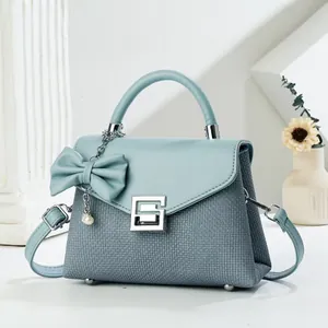 Detail of blue textured crossbody bag with silver lock, pearl charm and bow accessory