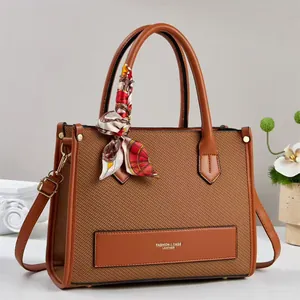 Detail of a brown woven tote bag with smooth leather trim and decorative silk scarf handle