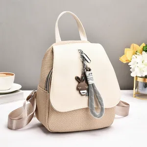 Beige woven texture backpack for women with rabbit pendant in bright indoor setting