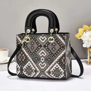 Detail of tweed tote bag with woven geometric pattern, metal charms, and leather strap