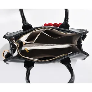Vue intérieure d'un sac à main en cuir verni noir avec compartiments et une fleur rouge