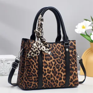 Detail of leopard print handbag featuring black leather trim and elegant silk scarf accent