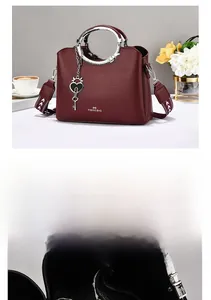 Detail of burgundy pebbled leather bag with circular metal handle and wide shoulder strap
