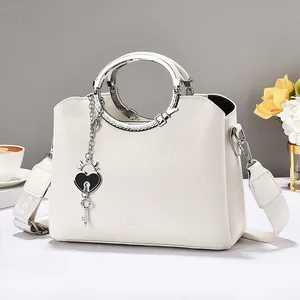 White lychee leather handbag with ring handle and heart charm on a decorative table