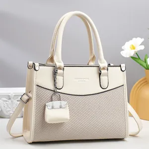 Detail of cream leather tote bag featuring woven texture and removable strap charm