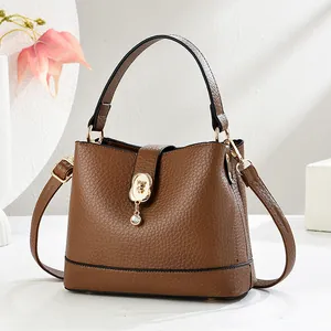 Sac seau en cuir marron avec boucle ours dorée et pendentif strass sur fond blanc épuré
