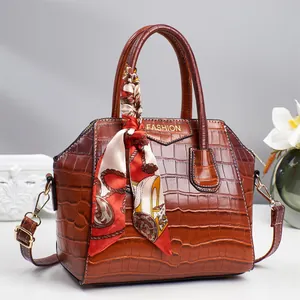 Braune Handtasche mit Krokodilprägung, Seidenschal und Fashion-Logo auf schlichtem Grund