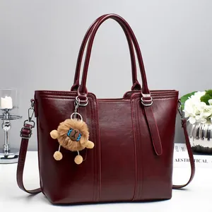 Detail view of burgundy bucket bag with vertical stitching and brown bear plush charm